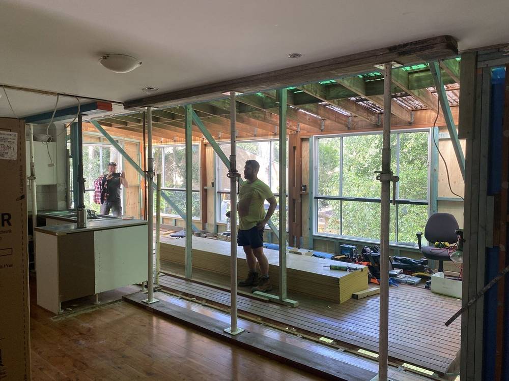 Carpenter inside a home with a wall opened up and propped