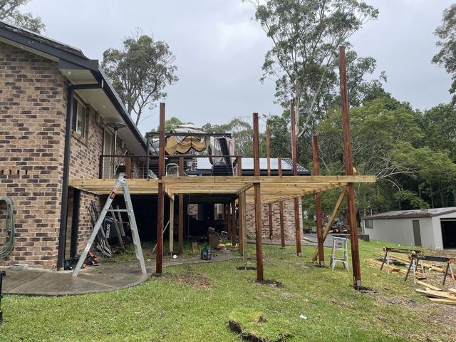 Timber posts and beams set up beside a brick house